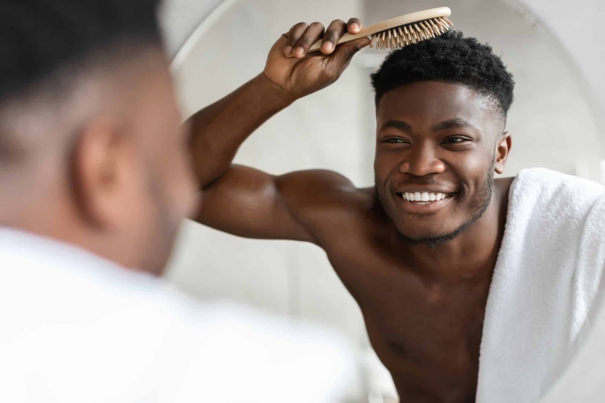 Cheerful Black Guy Brushing Short Hair With Hairbrush In Bathroom